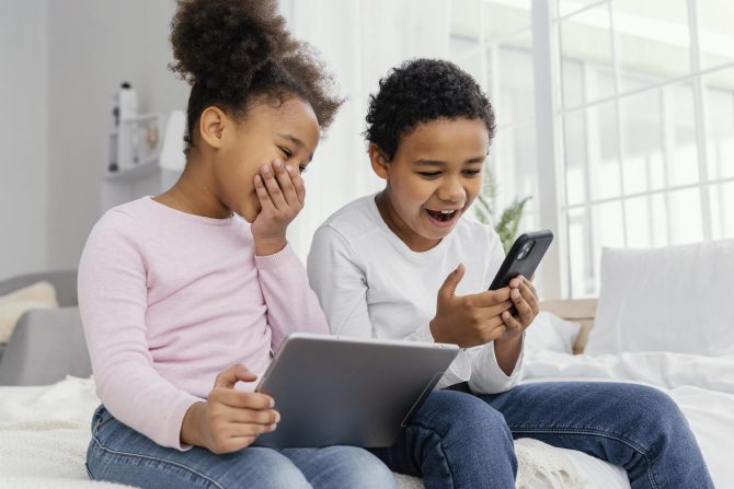 two-smiley-siblings-home-together-playing-tablet-smartphone